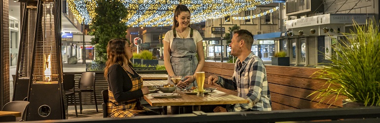 A photograph of a couple in a restaurant in outdoor seating at night being served by a waitress.