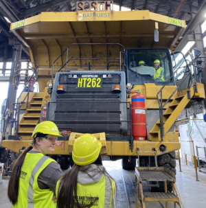 Photograph of gathering of students in orange high vis vests looking at large Bathurst mining machine