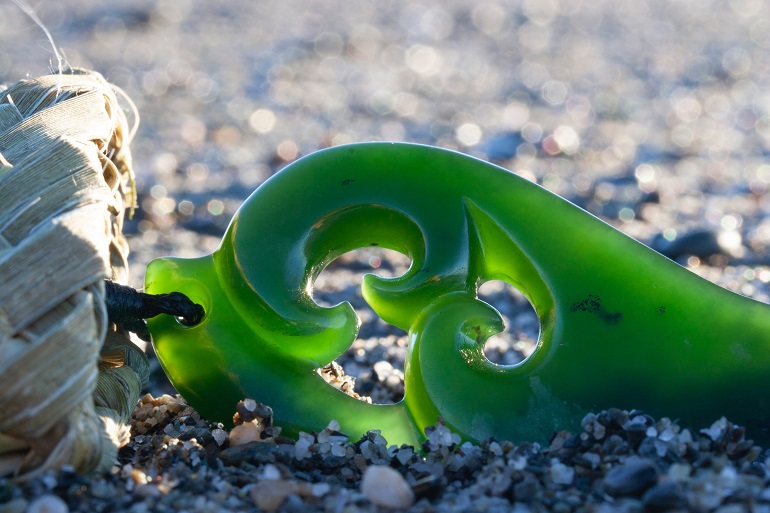 Close up photograph of a pounamu carving on a beach.