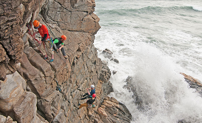 Rock climbers climbing a rocky face above a stormy sea.