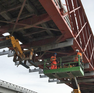 Photograph of two workers on the underside of a bridge being repaired 