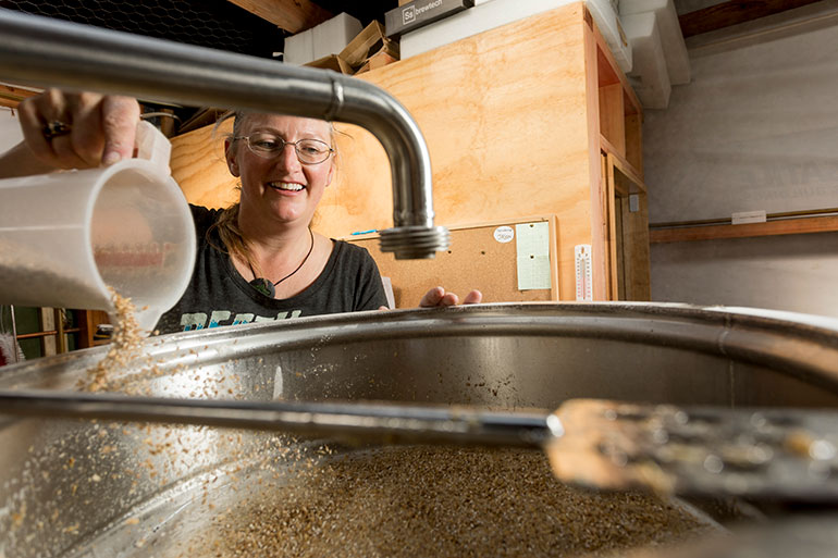 A woman pouring some grain into a big vat for beer brewing.