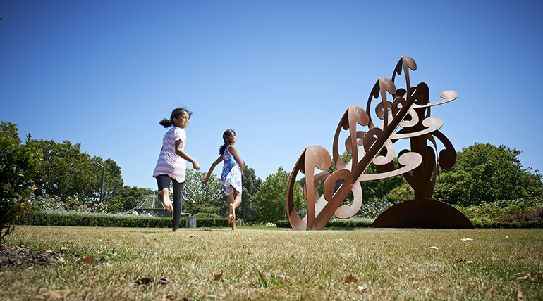 Visual of children running on grass in front of Mesh Sculpture