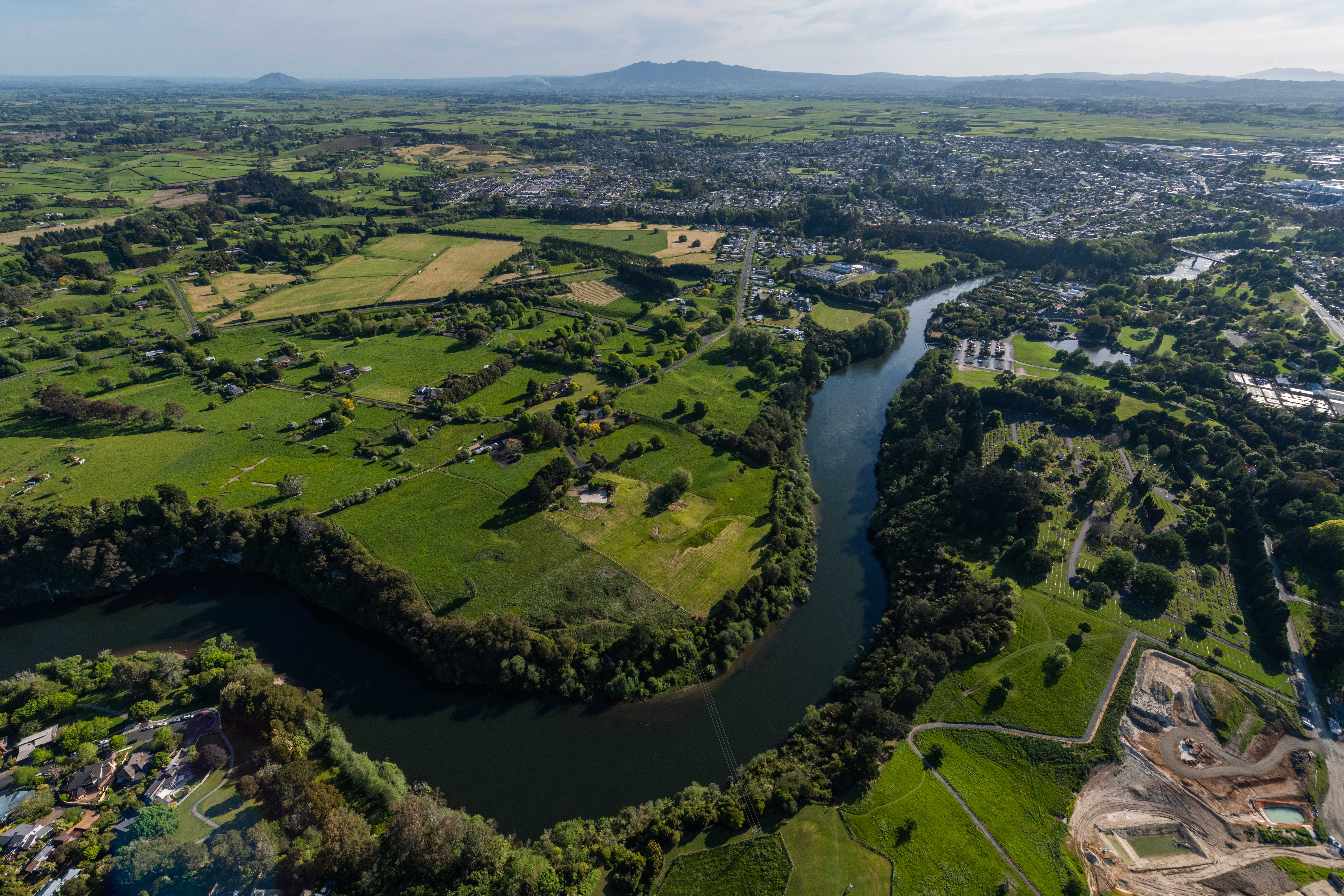 West-facing aerial view of Hamilton City with Waikato River and Hamilton Gardens in the foreground, and Mount Pirongia in the background