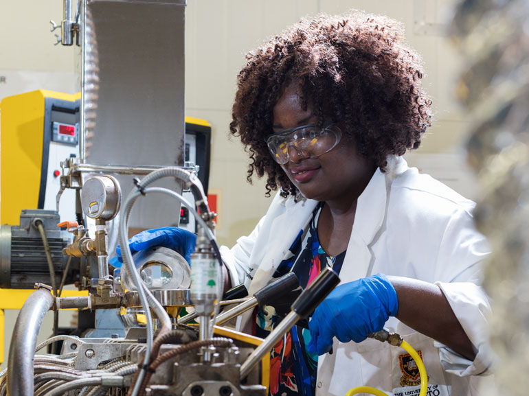 A person wearing a lab coat and safety glasses, and who is using a piece of equipment