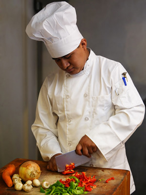Chef in white uniform and hat chopping vegetables.