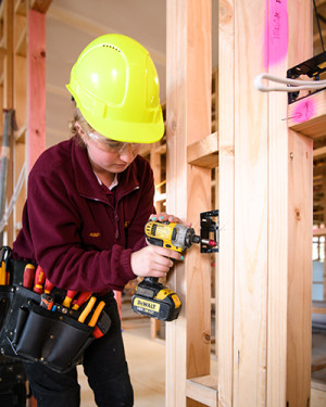 Woman in hard had drilling into wooden house framing.