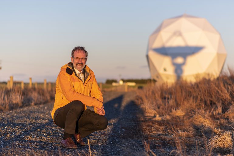 Robin Awarua crouching by Satellite Ground Station