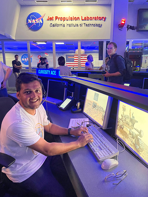 Photo shows Vivek sitting at a terminal at the Jet Propulsion Laboratory. The monitor shows the Mars Rover