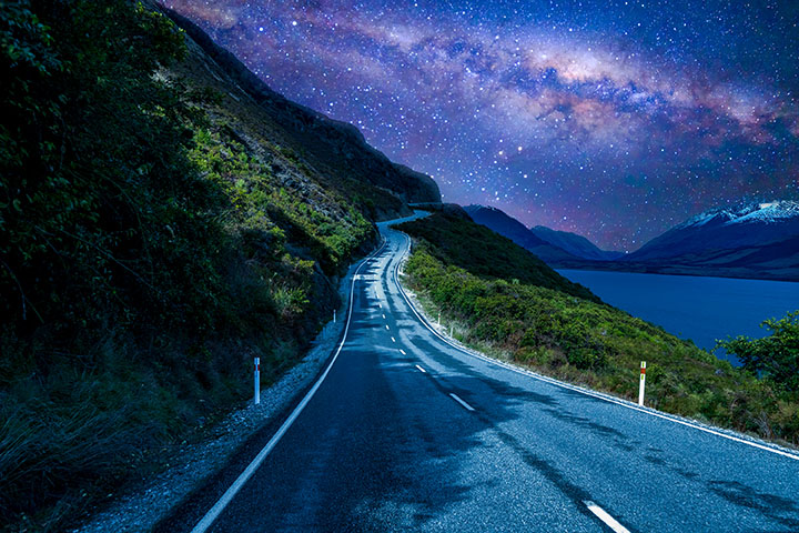 A road beside a lake at night. The milky way is visible in the night sky.