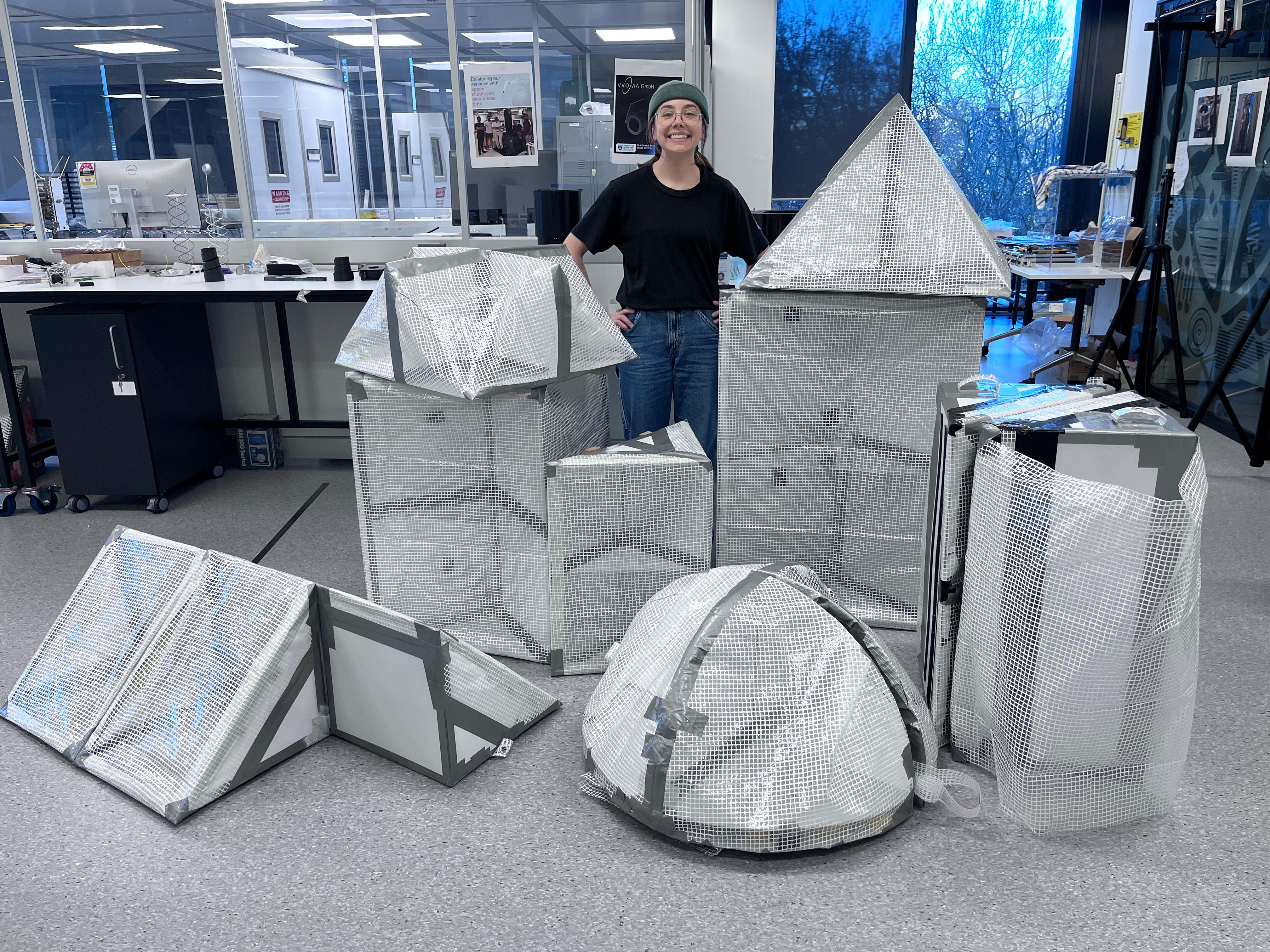 Ella Fasciana stands in the University of Auckland Space Institute, Fabrication and Assembly Facility surrounded by the full range of SAR4SAR Phase 2 prototypes, prior to testing in Omaha Bay, NZ.