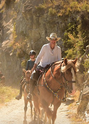 Two people riding horses up a dusty track.