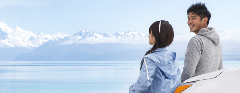 Couple leaning on car bonnet looking at mountains.