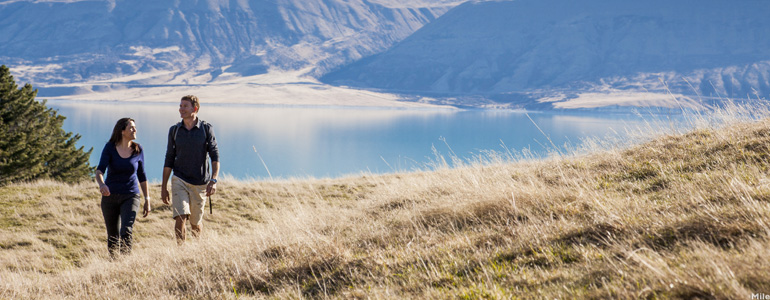 Couple walking on a grassy hill with lake and foothills in the background.