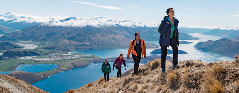 Trampers climbing a mountain with lakes and countryside in the background.