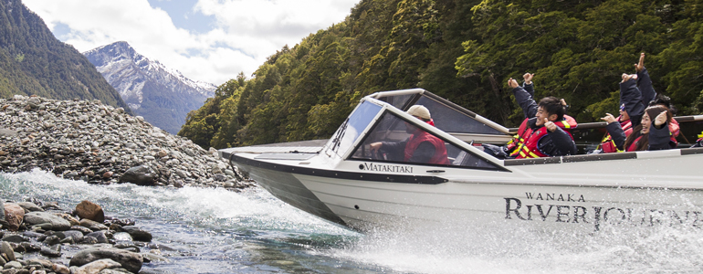 Tourists take a jetboat ride with mountains in the background.