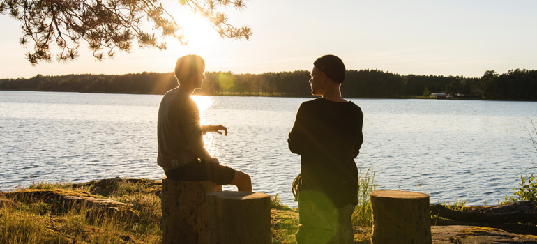 two people sitting by the water on tree logs