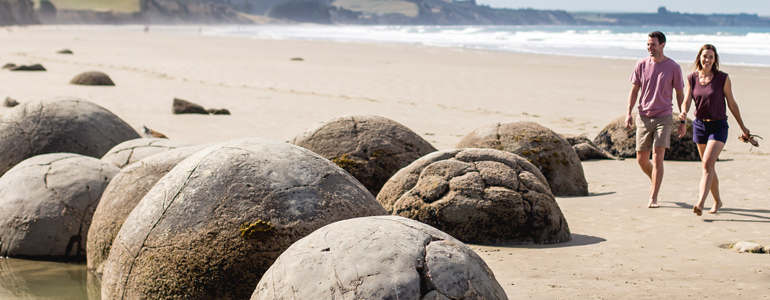 Couple walking at beach by Moeraki boulders.