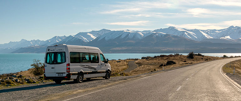 A campervan is parked on the roadside next to Lake Pukaki
