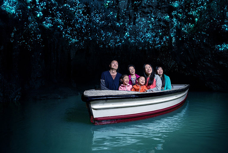 A family sits in a boat inside the Waitomo caves looking at the glow worms