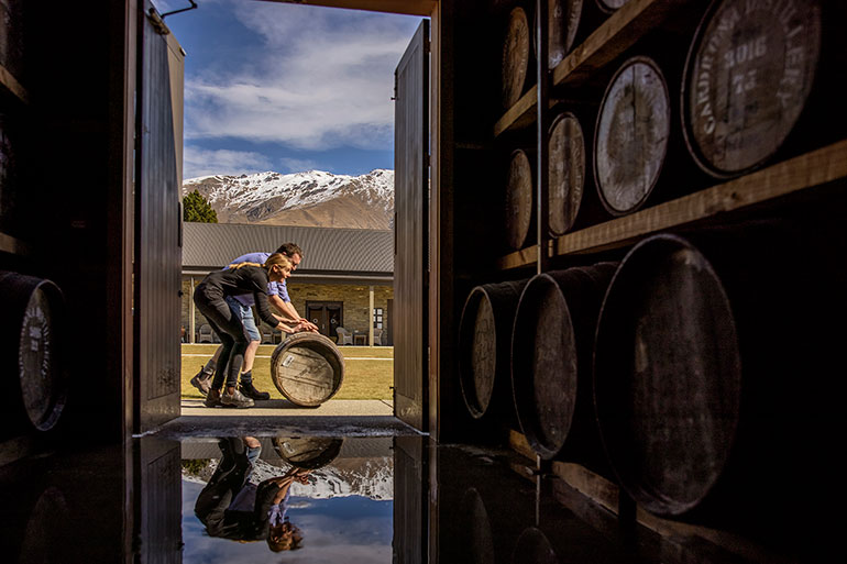 2 people rolling a barrel and Cardrona Distillery.