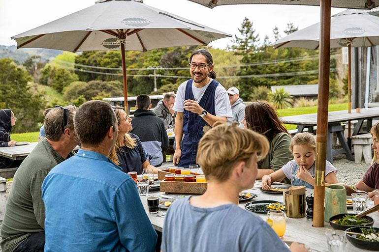 A hospitality worker interacting with clients as they enjoy their drinks and meals outdoors.  