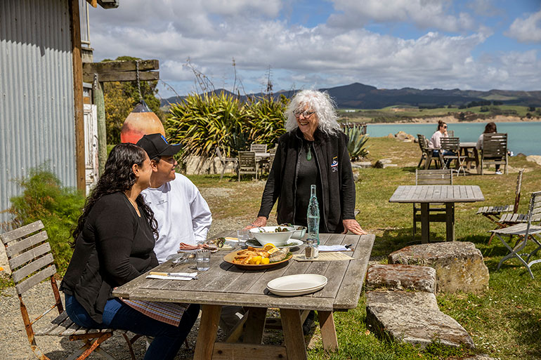 Guests dining at Fleur's in Moeraki with Fleur standing at their table.