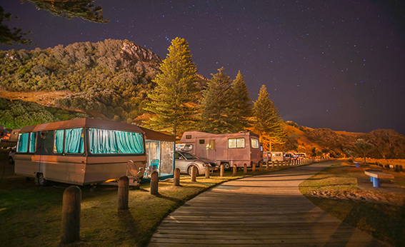 Caravans and mobile homes of holidaymakers under starry sky along wooden walkway to base of Mount Maunganui New Zealand