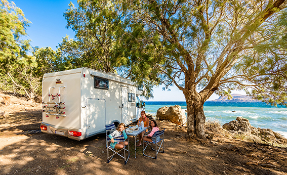 Family eating breakfast outside their motorhome under a tree
