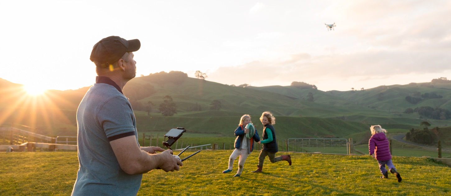 Farmer on lawn at sunset controlling drone with kids in the background