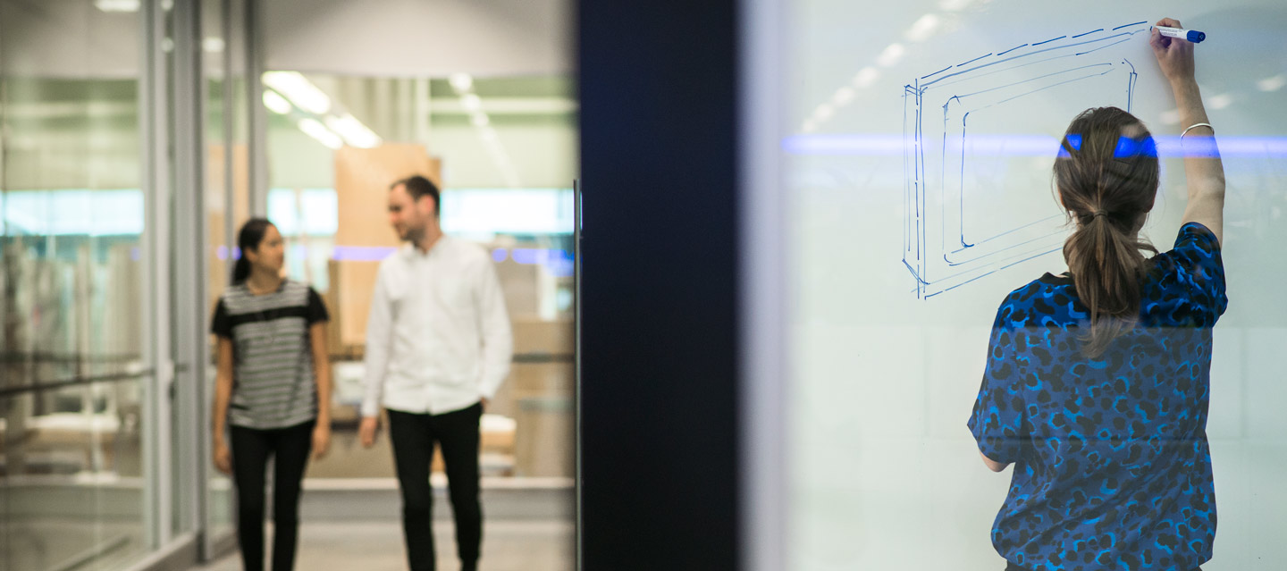 Left: 2 people walking down a corridor. Right: Person drawing on a whiteboard.